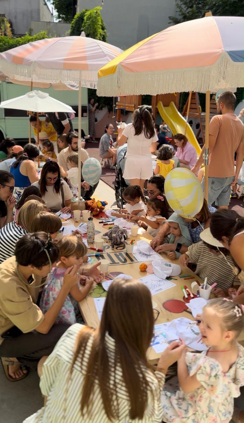 Atelier de desen în grădină: copii și părinți colorează împreună la o masă lungă, sub umbrele