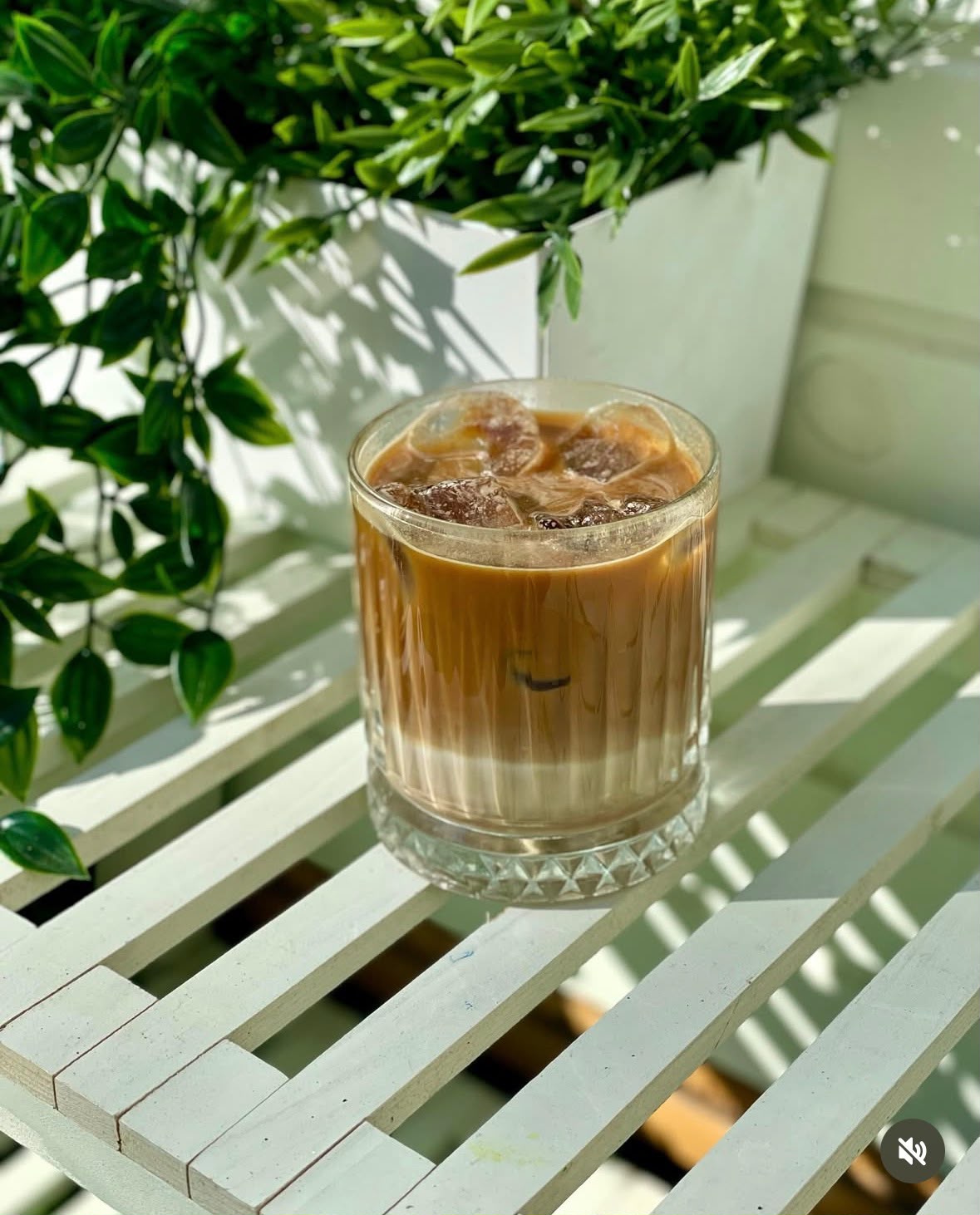 Cafea cu gheață și lapte într-un pahar striat, pe o masă albă din grădină